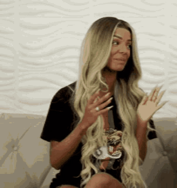 a woman with long blonde hair is sitting on a couch waving .
