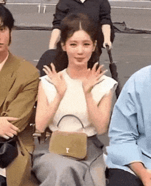 a woman is sitting in a chair with her hands up and a purse on her lap .