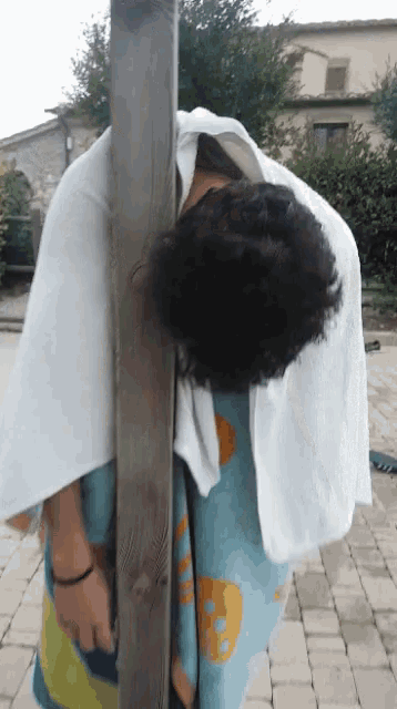 a person with a towel around their head is leaning against a wooden pole