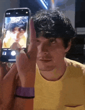 a man in a yellow shirt is taking a picture of himself on a cell phone