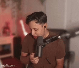 a young man is singing into a microphone while wearing headphones .