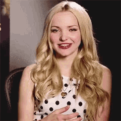 a blonde woman wearing a white polka dot dress smiles