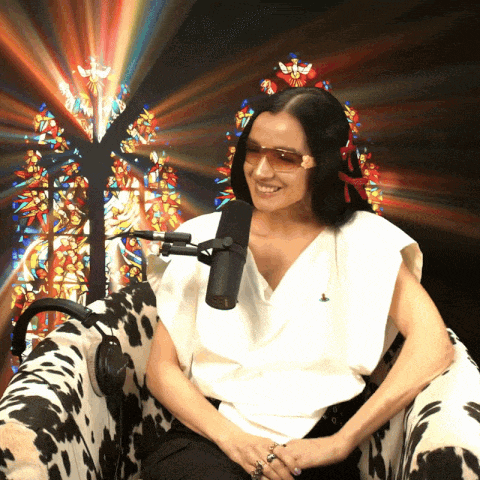 a woman wearing sunglasses is sitting in front of a microphone in front of a stained glass window