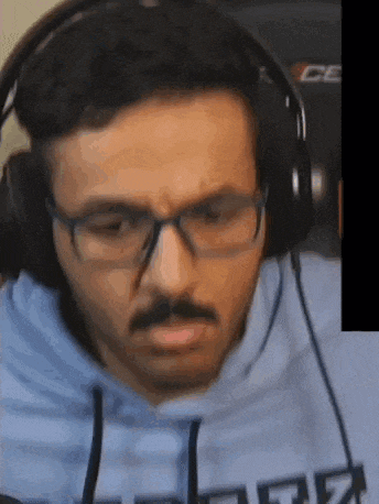 a man with glasses and headphones is wearing a blue hoodie and a mustache .
