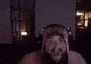 a man with a beard wearing headphones and a hoodie is sitting in a dark room .