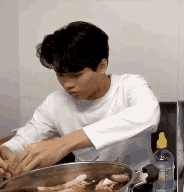 a young man is cooking food in a pot while sitting at a table .
