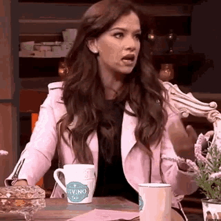a woman in a pink jacket is sitting at a table with a cup that says divino
