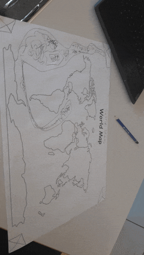 a drawing of a world map is on a desk next to a laptop