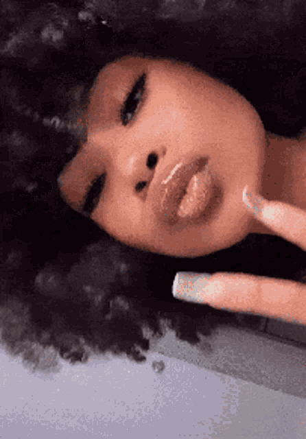 a close up of a woman 's face with a finger on her chin and a white nail .