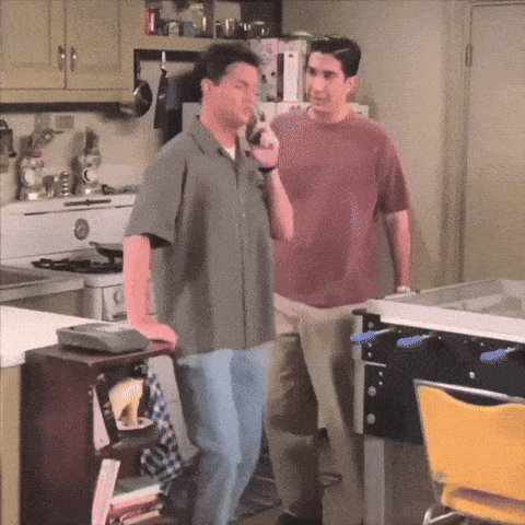 two men standing in a kitchen one talking on a phone