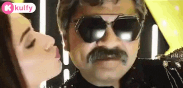 a woman is kissing a man with a mustache wearing sunglasses .