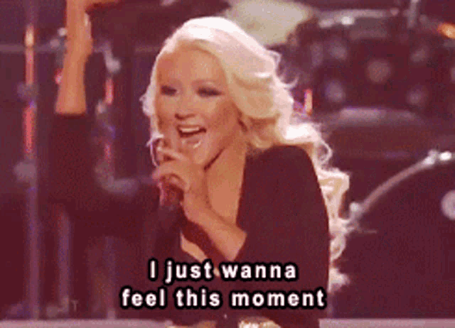 a woman singing into a microphone with the words " i just wanna feel this moment " below her