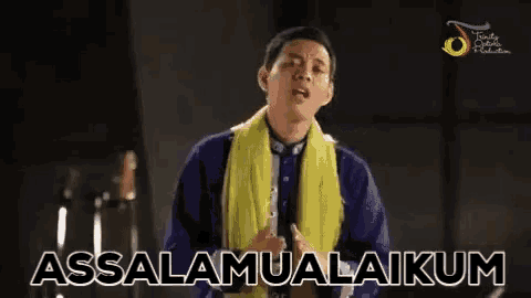 a man wearing a yellow scarf and a blue jacket is praying with the words assalamualaikum written on the screen behind him .