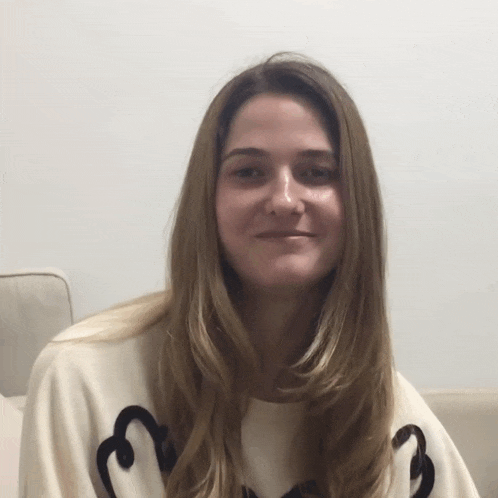 a woman wearing a white sweater with a black letter b on it smiles