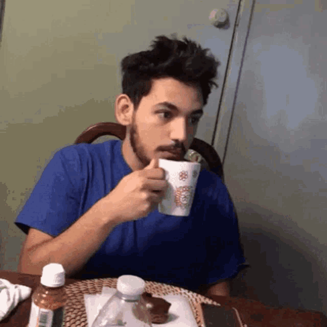 a man sitting at a table drinking from a cup