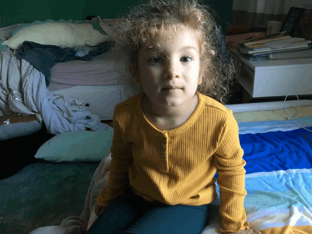a little girl wearing a yellow shirt is sitting on a bed