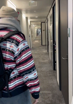 a man walking down a hallway with a backpack and a sweater that has the letter r on it
