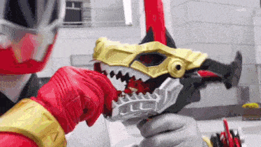 a person in a red and gold costume is holding a toy sword with a dinosaur head on it .