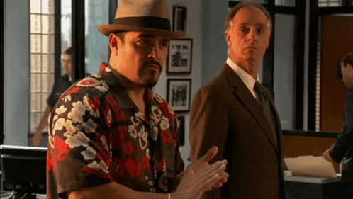 two men standing next to each other one wearing a hat