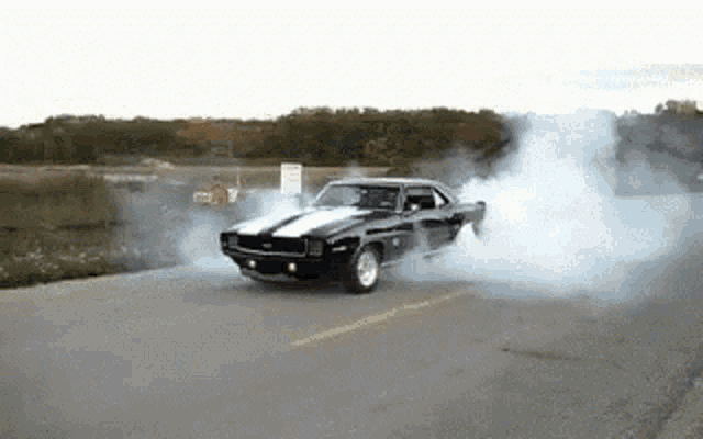 a black car with white stripes is doing a burnout on a road