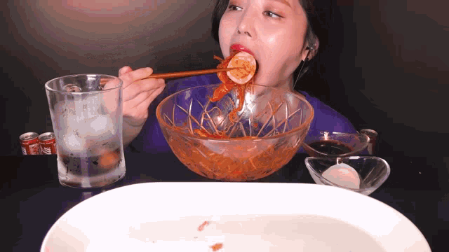 a woman is eating a bowl of food with chopsticks next to a glass of coca cola