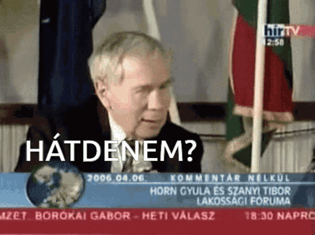 a man in a suit and tie is sitting in front of a television screen that says hatdenem