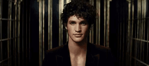 a young man with curly hair is standing in front of a mirror .