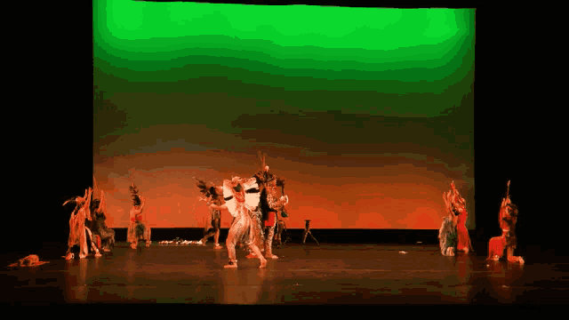 a group of dancers on stage with a green screen behind them
