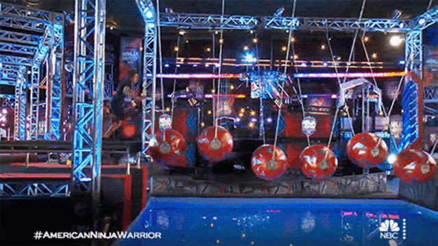 a person is hanging from a rope in a ninja warrior arena
