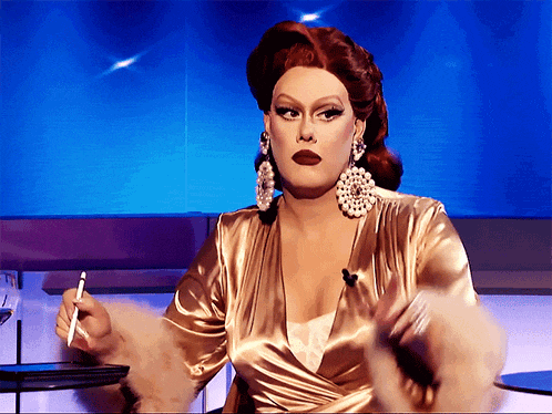 a drag queen is holding a pen in her hand while wearing pearl earrings