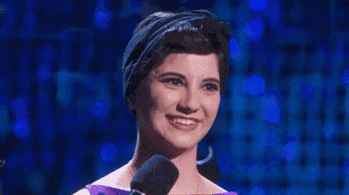 a woman is smiling while standing in front of a microphone on a stage .