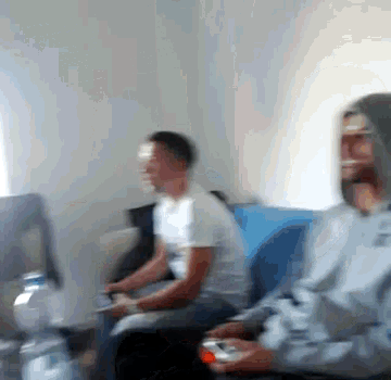 two men are sitting on a blue couch playing a video game