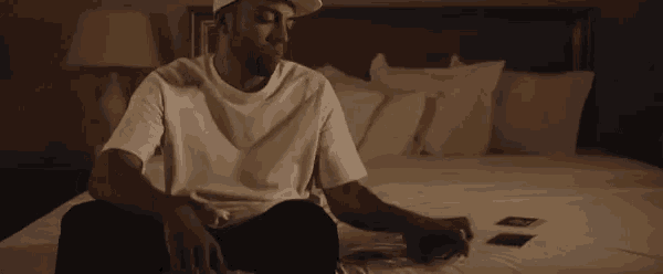 a man in a hat is sitting on a bed looking at photos .