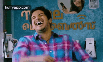 a man in a plaid shirt is laughing while sitting at a desk .