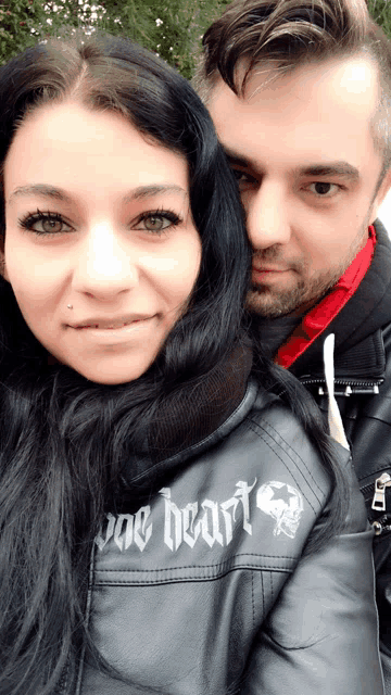 a man and a woman are posing for a picture and the woman is wearing a jacket that says " one heart "