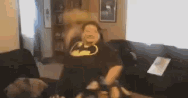 a man in a batman t-shirt is dancing in a living room .