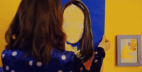 a woman in a blue polka dot dress is painting a picture of herself on a yellow wall .