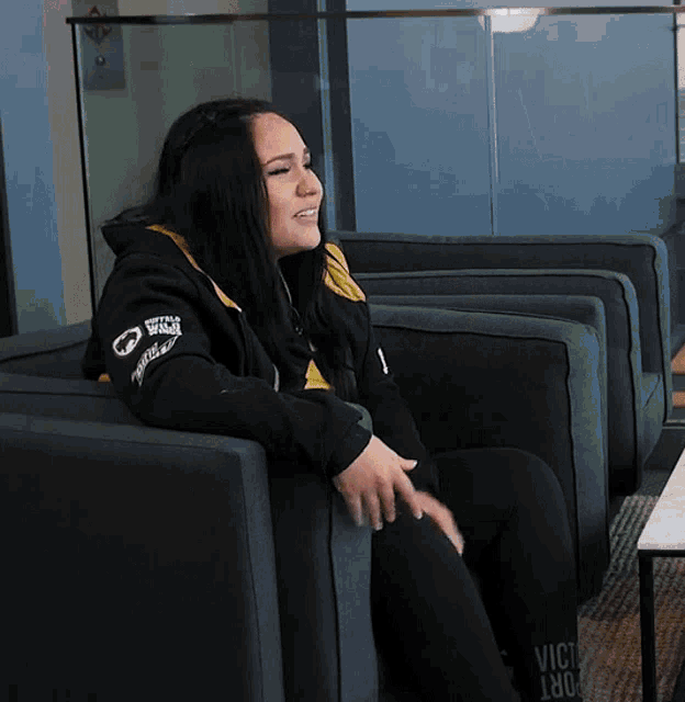 a woman sits in a chair wearing a black jacket that says victory