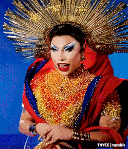 a drag queen is wearing a red and gold outfit and a gold crown