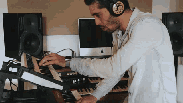 a man wearing headphones plays a keyboard in front of an apple computer