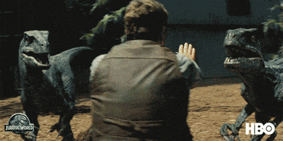 a man 's hand is reaching out in front of a jurassic world sign