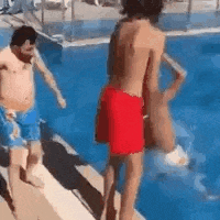 a man in red shorts is standing next to a swimming pool .