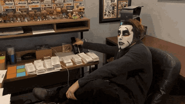 a man wearing a mask sits at a desk with stacks of bills on it