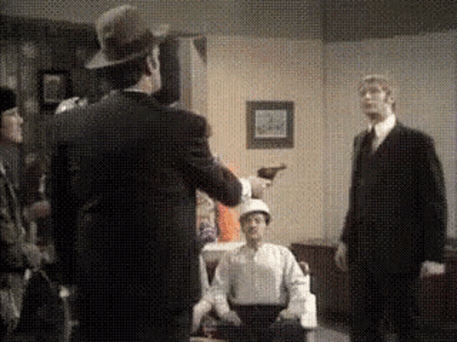 a man in a hat is pointing a gun at another man in a suit and tie .