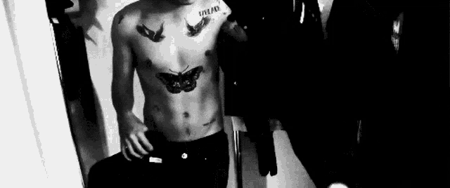 a man with a butterfly tattoo on his chest is taking a selfie in front of a mirror .