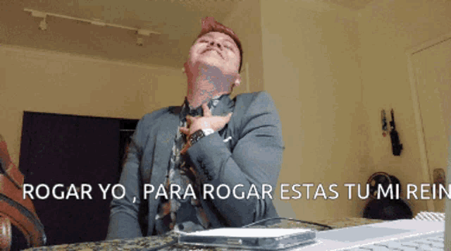 a man in a suit and tie is sitting in front of a laptop with the words " rogar yo " on the bottom