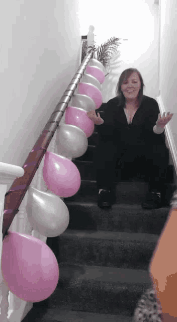 a woman is sitting on a set of stairs with pink and silver balloons hanging from the railing