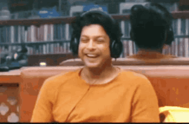 a man wearing headphones is sitting on a couch laughing .