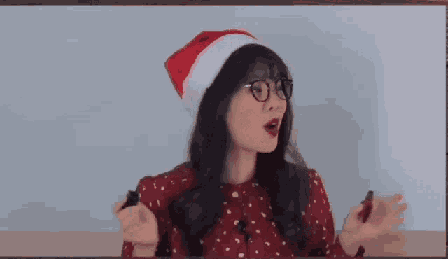 a woman wearing a santa hat and glasses holds a bottle of lipstick