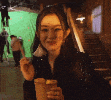 a woman is sitting in front of a green screen holding a cup of coffee and a piece of fruit .